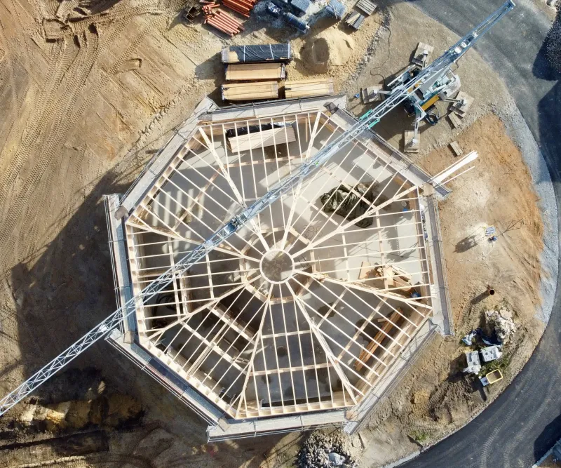 Luftaufnahme einer achteckigen Dachkonstruktion aus Holzrahmenbau während der Bauphase – präzises Handwerk und nachhaltige Bauweise.