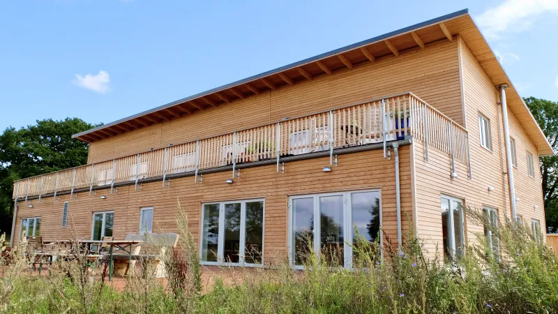 Modernes Mehrfamilienhaus mit Holzfassade und großem Balkon, gebaut in nachhaltiger Holzrahmenbauweise – ökologisches und energieeffizientes Wohnen.