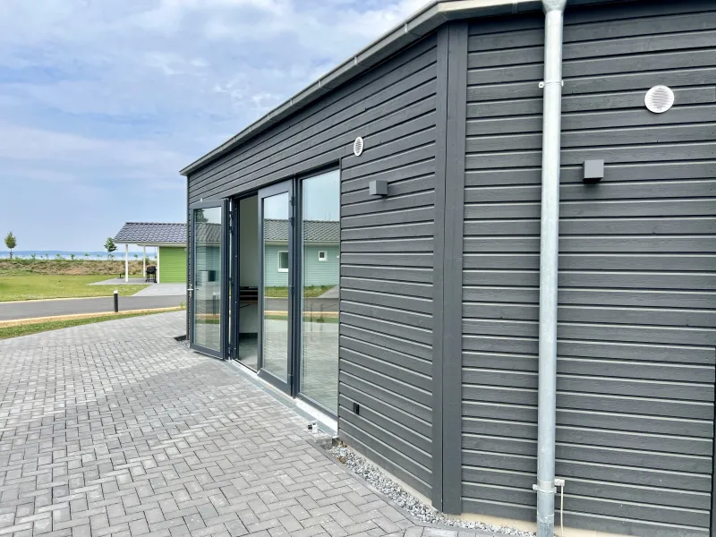 Großflächige Fenster öffnen den Innenraum zur Natur. Die edle Holzfassade in dunklem Grau kombiniert Nachhaltigkeit mit moderner Gestaltung – ideal für Veranstaltungen mit Anspruch.