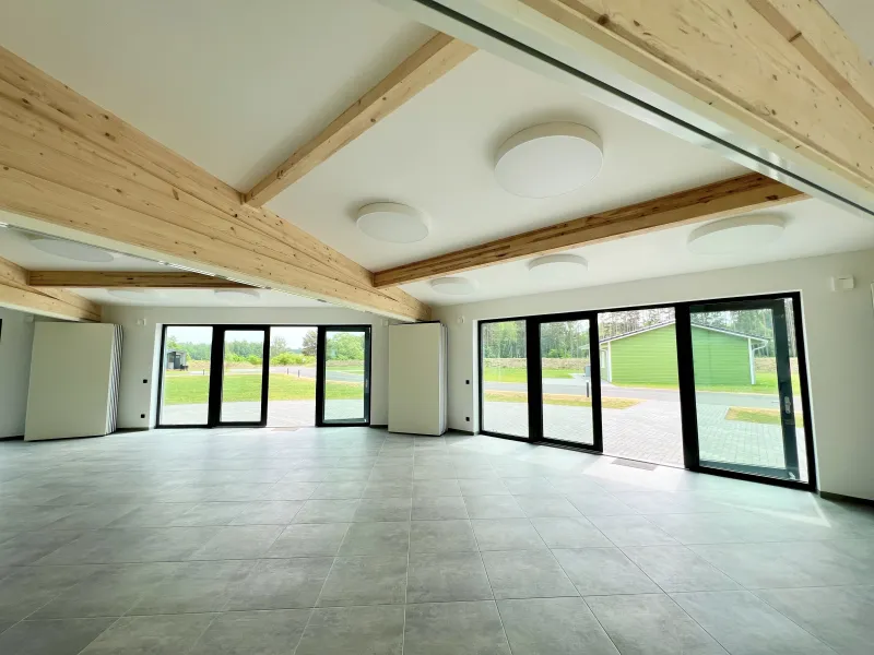 Großer, lichtdurchfluteter Raum mit sichtbaren Holzbalken und bodentiefen Fenstern in moderner Holzrahmenbauweise – nachhaltige Architektur mit natürlicher Atmosphäre.