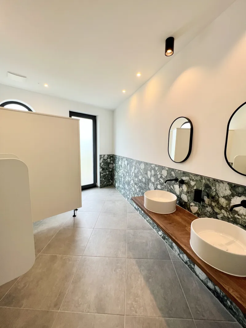 Helles, modernes Badezimmer mit Natursteinverkleidung, zwei Designer-Waschbecken und minimalistischer Architektur – hochwertiges Interieur im nachhaltigen Hausbau.